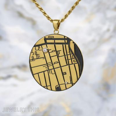 Round gold map pendant with engraved lines, black inlay, and two small round stones on a gold chain