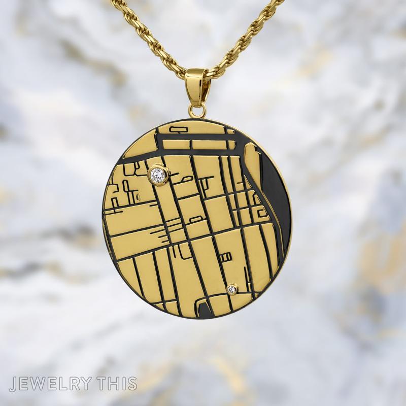 Round gold map pendant with engraved lines, black inlay, and two small round stones on a gold chain
