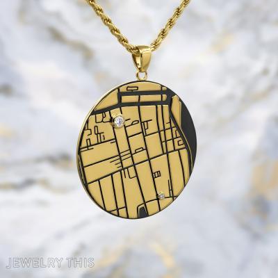 Round gold map pendant with engraved lines, black inlay, and two small round stones on a gold chain