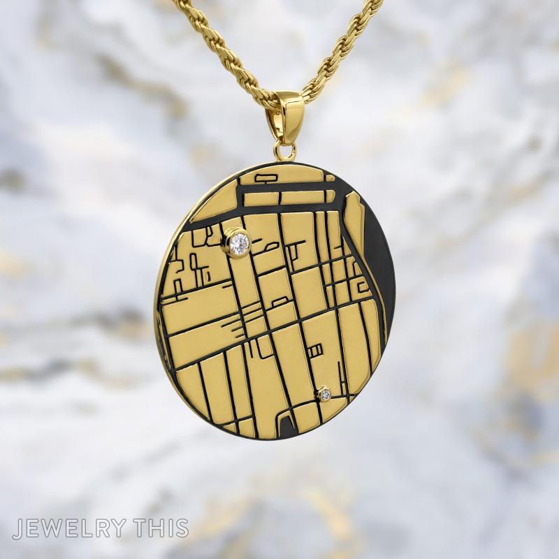 Round gold map pendant with engraved lines, black inlay, and two small round stones on a gold chain
