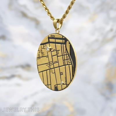 Round gold map pendant with engraved lines, black inlay, and two small round stones on a gold chain
