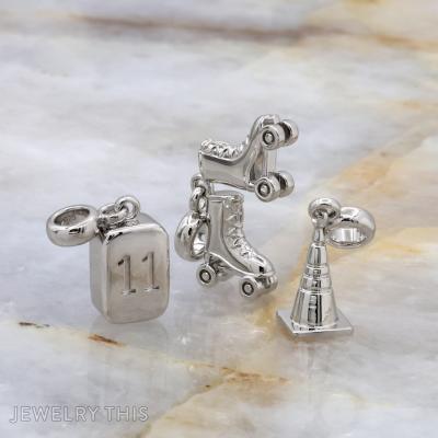 Three-dimensional silver charms shaped as a number block, roller skate, and construction cone.