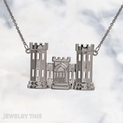A sterling silver pendant shaped like a two-tower castle with a central gatehouse, featuring cut-out rectangular windows and crenellated tops, hanging from a silver cable chain against a marble background.
