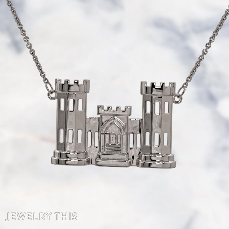 A sterling silver pendant shaped like a two-tower castle with a central gatehouse, featuring cut-out rectangular windows and crenellated tops, hanging from a silver cable chain against a marble background.