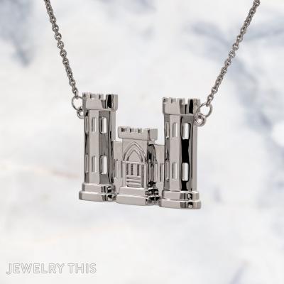 A sterling silver pendant shaped like a two-tower castle with a central gatehouse, featuring cut-out rectangular windows and crenellated tops, hanging from a silver cable chain against a marble background.